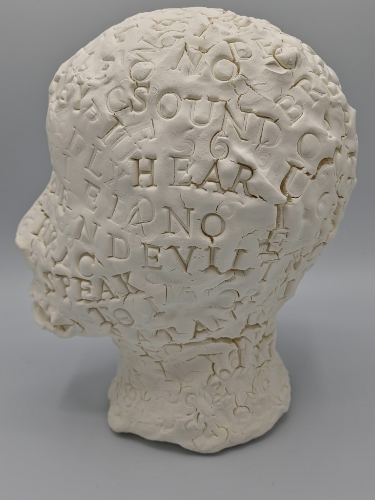 Clay Head #4 Left profile 
text includes gouged stamped words: HEAR DEVIL SPEAK NO scattered in wave patterns over the clay head.